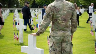 A soldier in fatigues stands next to a headstone. 